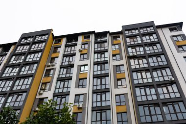 Siyah ve sarı cepheli uzun konut yapısı, bir şehirde grimsi bir gökyüzüne karşı sayısız pencere ve havalandırma ünitesi içerir..