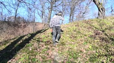 Bir insan elinde kamerayla çimenli bir yamaca tırmanıyor, güneşin sıcaklığının tadını çıkarırken ağaçlar dik duruyor, ilkbaharın gelişini kutluyorlar..