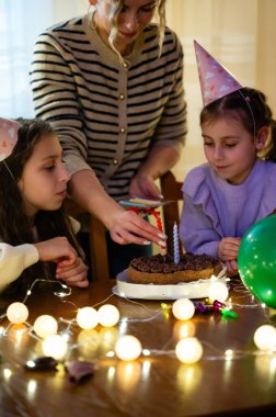 Çocuklar güzel dekore edilmiş bir pastanın etrafında toplanırken bir bakıcı mumları yakıp büyülü bir neşe anı yaratırken doğum günü kutlaması kahkahalarla dolu.
