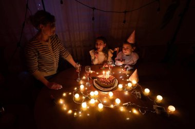 Neşeli bir kutlama, çocuklar bir pastanın üzerinde mum yakarken etrafında parıldayan peri ışıkları ve sıcak kahkahalar, sıcak bir atmosferde sevgi dolu anılar yaratırken gerçekleşiyor..