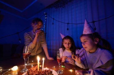 Üç kız, sıcak ışık ve neşe dolu dekorasyonlarla çevrili, ikram ve içeceklerle kutluyor. Kahkaha ve arkadaşlık bu özel gecede havayı dolduruyor..