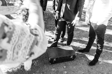 Toplantının siyah beyaz fotoğrafı. Zeminde yıpranmış bir bavul duruyor, muhtemelen olay için önemli. Resmi giysili insanlar etrafını sarmış, bir ayin ya da etkinlik öneriyorlar..