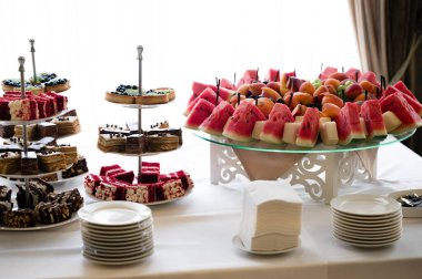 Lezzetli bir hamur işi, dilimlenmiş karpuz, şeftali ve zarif bir ziyafet ya da parti için diğer meyveler. Tabaklar ve peçeteler yakınlarda..