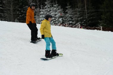 İki snowboardcu, yemyeşil ağaçlarla çevrili karlı bir yamaçta süzülüyor. Neşe ve heyecan dolu serin kış harikalar diyarında yeteneklerini sergiliyorlar..
