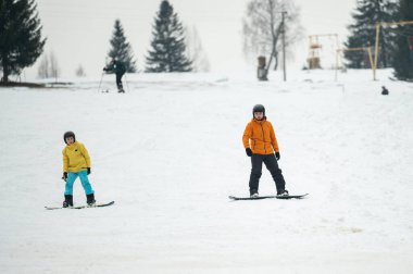 Snowboardcular, yüksek çam ağaçları ve coşkulu bir neşe ve heyecan atmosferiyle çevrili bir kış otelinde, karlı bir yamaçta heyecanlı bir günün tadını çıkarıyorlar..