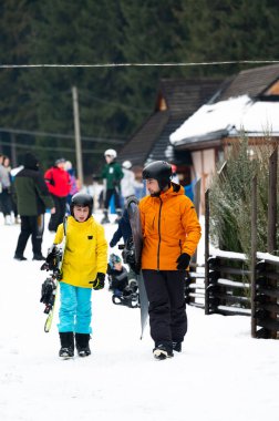 Parlak giyimli kar meraklıları karlı bir patika boyunca mutlu bir şekilde yürürler. Kış sporcularıyla dolu canlı bir dağ otelindeki yamaçlara vurmaya hazırdırlar..