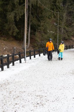 Kayak meraklıları, renkli kış giysileri içinde, karlı bir patika boyunca yürüyüp yumuşak bulutlarla dolu gri bir gökyüzünün altında dingin dağ atmosferini alırlar..