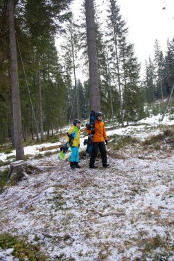 İki snowboardcu, bir çocuk ve bir yetişkin, görkemli çam ağaçları ve taze karla çevrili karlı bir ormanda maceralı bir güne hazırlanıyorlar..
