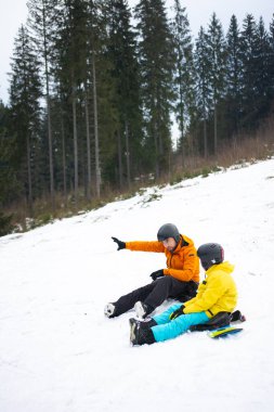 Baba ve çocuk, güzel bir kış manzarasında bir sonraki snowboard koşularını tartışırken uzun yeşil ağaçlarla çevrelenmiş bir şekilde neşeli bir anı paylaşıyorlar..