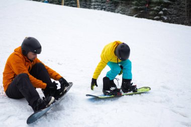 İki hevesli snowboardcu kar kaplı bir yamaçta süzülmeye hazır, yüksek yeşil ağaçlar serin bir kış gününde çarpıcı bir zemin sağlıyor..