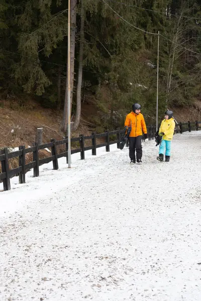 Kayak meraklıları, renkli kış giysileri içinde, karlı bir patika boyunca yürüyüp yumuşak bulutlarla dolu gri bir gökyüzünün altında dingin dağ atmosferini alırlar..