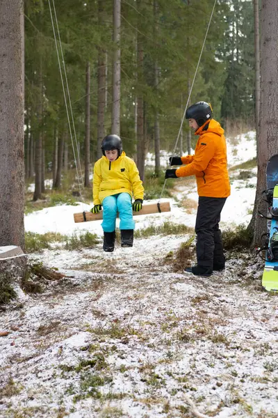 İki arkadaş, uzun ağaçlarla çevrili karlı bir ormanda sallanarak, serin bir öğleden sonra eğlencenin ve dostluğun özünü yakalayan neşeli bir anın tadını çıkarırlar..