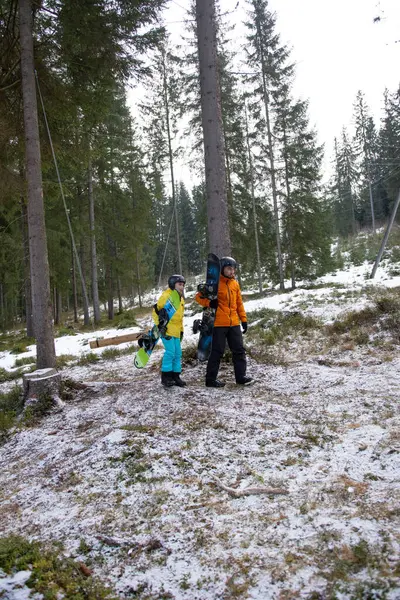 İki snowboardcu, bir çocuk ve bir yetişkin, görkemli çam ağaçları ve taze karla çevrili karlı bir ormanda maceralı bir güne hazırlanıyorlar..