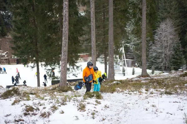 Çocuklar yüksek ağaçlar ve heyecanlı kış sporları meraklılarıyla çevrili snowboard sporunu öğrenirken aileler bir kayak merkezinin karlı yamacında toplanıyor..