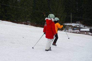 Renkli giysiler içinde iki genç kayakçı bir dağ yamacında süzülüyor, eğlence dolu bir kış gününün tadını çıkarırlarken yeteneklerini ve heyecanlarını sergiliyorlar..