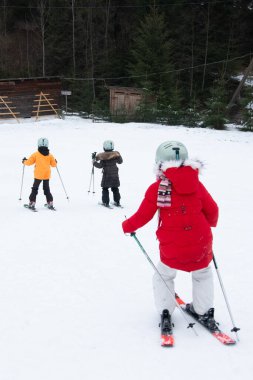 Çocuklar, parlak renkli kıyafetlerle el değmemiş karla zıt düşerek kayak günlerinin tadını çıkarıyorlar. Yokuştan aşağı süzülürken huzurlu atmosferde kahkahalar yankılanıyor..