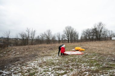 Sessiz bir kış ortamında, bireyler yapraksız ağaçlarla çevrili bir paraşüt kurmak için birlikte çalışırlar ve kar tozu çekerek maceranın ruhunu yakalarlar..