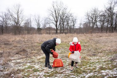 İki çocuk, çıplak ağaçlar ve çimlerle çevrili soğuk, kış manzarasında keşif ve heyecan için sıcak giyinmiş bir maceraya hazırlanıyor..