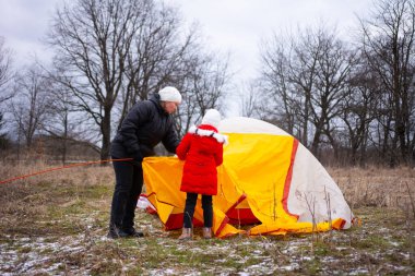 Sıcak giyimli iki insan, soğuk bir öğleden sonra neşeli ve maceralı bir atmosfer yaratmak için, karlı bir arazide parlak bir çadır kurmak için birlikte çalışırlar..