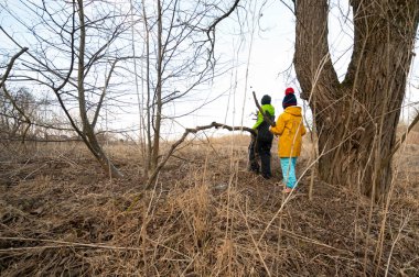 İki arkadaş, renkli ceketlerle sarılı, sessiz bir ormanda, ilkbaharın serinliğini kucaklayan narin dalları ve topraksı dokuları fark ederek maceraya atılırlar..