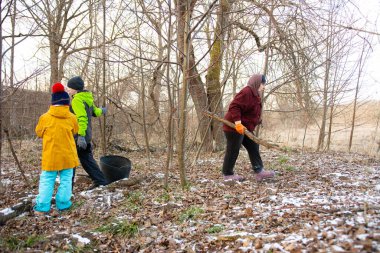 Sakin bir kış ortamında, yetişkinler ve çocuklar çıplak ağaçlar ve açık havada düşen yapraklarla çevrili çubukları toplamak için birlikte çalışırlar..