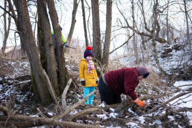 İki çocuk ve bir yetişkin, karlı bir ormanda kış gezintisinin tadını çıkarıyorlar. Çubukları topluyorlar ve huzurlu bir dere kenarındaki çevreyi keşfediyorlar..