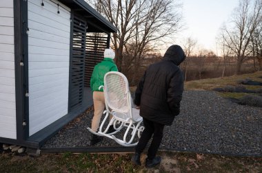 Bir sallanan sandalyeyi antika bir kulübeye doğru hareket ettiren iki kişi, alacakaranlıkta huzurlu kırsal titreşimleri vurgulayan sakin bir parıltı yayarken çakıl arazisinde geziniyor..