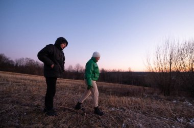 Arkadaşlar alacakaranlıkta sakin bir arazide yürürler, kalın ceketlerle sarmalanmışlardır. Gün batımının yumuşak parıltısı kışın ortasında sakin bir atmosfer yaratır..