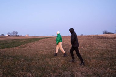 İki arkadaş, alacakaranlıkta, gün geceye dönerken doğanın sükunetiyle çevrili açık bir arazide yan yana yürürler..