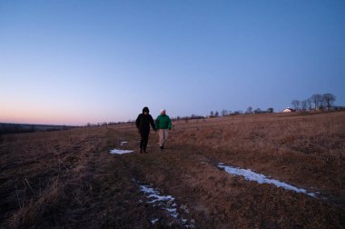İki birey, alacakaranlıkta sakin bir çayırda yan yana yürürler. Gündüzün kışın geceye dönüşmesi gibi doğanın huzurunun tadını çıkarırlar..