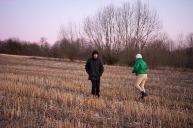Alacakaranlık ışığı altında, iki kişi huzurlu bir arazide geziniyor, serin havanın ve etraflarındaki manzaranın sessiz güzelliğinin tadını çıkarıyorlar..