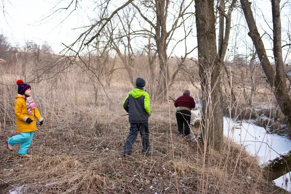 Serin bir öğleden sonra çocuklar, çıplak ağaçlar ve uzun otlarla çevrili derenin kıyısında kışın kucakladığı macera ruhunu kucaklayarak neşeyle koşar..