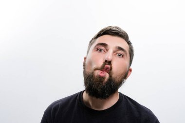 Sakallı bir adam, beyaz bir arka plana komik bir yüz çizer. Neşeli bir ifadeyle dudaklarını büzüyor..