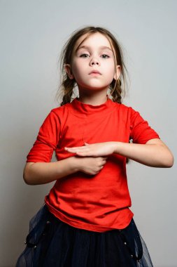 Kırmızı gömlek ve koyu tüllü etek giyen at kuyruklu genç bir kızın portresi. Basit bir arka fona karşı duruyor, elleri önünde sıkıca bağlı..