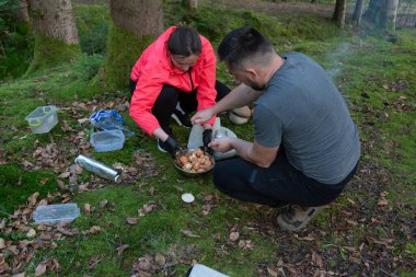 Gün batımında sakin bir orman açıklığında, bir çift lezzetli bir yemek pişirmekle meşgul. Açık havada güzel vakit geçirirken huzur ve manzaranın tadını çıkarıyorlar..