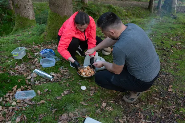 Gün batımında sakin bir orman açıklığında, bir çift lezzetli bir yemek pişirmekle meşgul. Açık havada güzel vakit geçirirken huzur ve manzaranın tadını çıkarıyorlar..