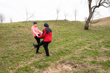 İki arkadaş, serin ve bulutlu bir günde ağaçlarla çevrili güzel bir çimenlikte dans ederken gülüşlerini ve hareketlerini paylaşıyor..