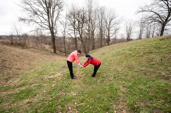 Dostlar, serin bir bahar gününde, yuvarlanan tepeler ve çıplak ağaçlarla çevrili sakin doğal ortamda, keyifli, ortak bir esneme egzersizi yaparlar..
