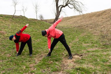Sakin bir açık havada, iki insan esneme rutinleri uyguluyor, esnekliklerini artırıyor ve doğal manzaranın ortasında sağlıklarını geliştiriyor..