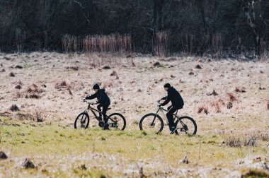 Dağ bisikletleriyle gezen iki birey sakin bir arazide, doğanın huzuru içinde huzurlu bir doğa deneyimi yaşıyor. Manzara sakin ve davetkar..