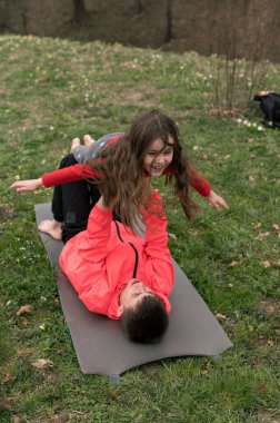 İki çocuk yoga minderinde neşeli pozlar verirken neşeli anlar paylaşılır. Canlı yeşillik ve kaygısız bir eğlence ve bağ hissi ile çevrelenir..