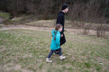 Genç bir kız, büyük bir oğlanın yanında yürüyor. İkisi de serin bir bahar gününde serin ve ferahlatıcı bir doğa yürüyüşünün tadını çıkarıyor..