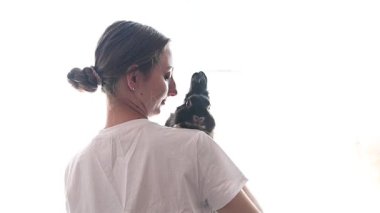 Güzel bir kız pencerenin yanında duruyor ve evcil tavşanıyla oynuyor, dekoratif siyah bir tavşan..