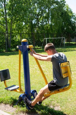 Genç bir insan açık hava spor salonunda bacak pres makinesi kullanıyor. Sahne parlak ve güneşli. Aktif ve sağlıklı bir yaşam tarzı sergiliyor..