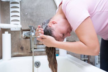 Banyoda bir kadın yakalanmış, küvetin üzerine eğilmiş, uzun saçlarını yıkıyor. Sabun köpükleri aşikar. Küvetin arkasında çıplak su tesisatı var. O pembe bir gömlek giyiyor..