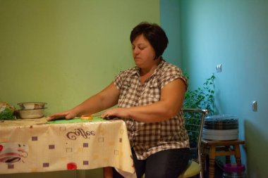 Bu resim, sıcak bir mutfakta tatlı hazırlamaya odaklanmış bir kadını gösteriyor. Masa desenli bir kumaşla süslenmiş. Sahneye biraz ahlâksızlık katıyor..