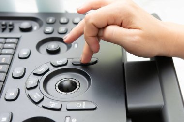 Operatörün parmağının düğmeye basmasına odaklanmış siyah bir ultrason makinesini çalıştıran elin yakın çekimi. Ayarlar klinik, kontrol paneli var..