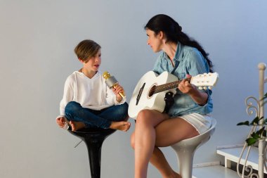 Genç bir çocuk bir mikrofon tutuyor ve annesinin beyaz bir akustik gitarı tıngırdattığı gibi şarkı söylüyor. Taburelere oturup gündelik bir müzik seansının tadını çıkarıyorlar..