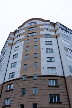 Çok katlı bir binada, bulutlu gökyüzüne karşı dimdik duran renkler ve dokuların bir karışımı sergilenirken şehir ayarı aşağıdaki yaşamla uğulduyor..