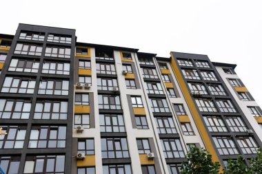 Parlak, modern konut yapısı bulutlu bir gökyüzüne karşı dimdik ayakta duruyor, büyük pencereli cesur mimari, doğal ışığı konutlara davet ediyor..